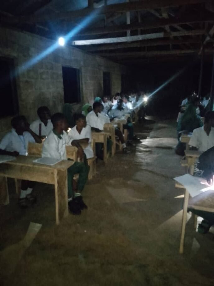 WAEC candidates writing examination papers at night using torchlights and phone flashlights after delays in the arrival of exam materials.