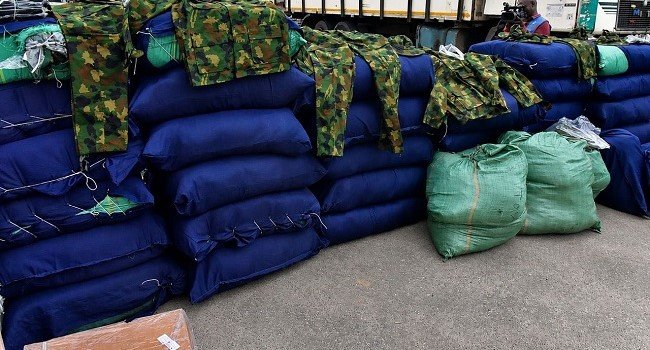 Police officers display 47 sacks of intercepted military camouflage uniforms and cartons of suspected illicit substances seized during an operation in Lagos.