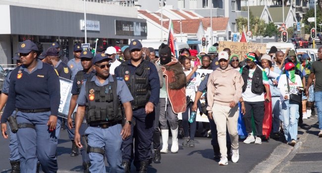 South African police officers escort anti-illegal immigration protesters carrying national flags during a march in Cape Town ahead of a June 30 migrant deadline.
