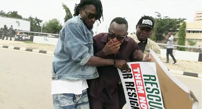 Protesters dispersing in Abuja after police fired teargas during a Democracy Day demonstration, with Omoyele Sowore seen receiving assistance from others.