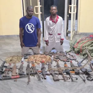 DSS and Nigerian Army operatives displaying recovered AK-47 rifles, ammunition and NYSC uniforms seized during a raid in Enugu State.