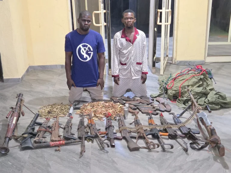 DSS and Nigerian Army operatives displaying recovered AK-47 rifles, ammunition and NYSC uniforms seized during a raid in Enugu State.
