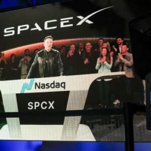 Elon Musk speaking at a SpaceX launch event in Starbase, Texas, displayed on a screen during the company’s Nasdaq IPO debut as shares surge following record-breaking public offering.