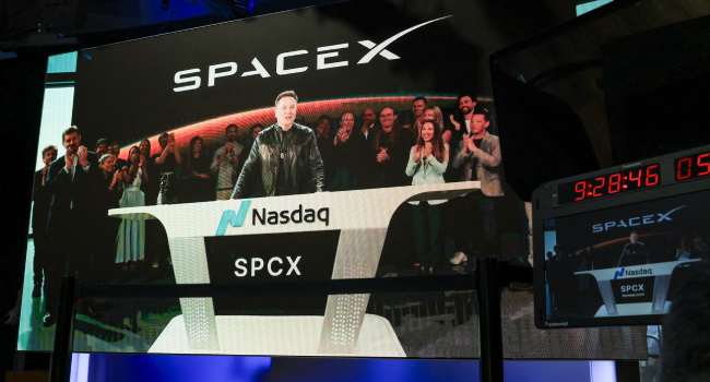 Elon Musk speaking at a SpaceX launch event in Starbase, Texas, displayed on a screen during the company’s Nasdaq IPO debut as shares surge following record-breaking public offering.