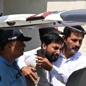 Grieving father consoles another parent as a child's coffin is carried outside PIMS Hospital following a fire that killed 14 infants in Islamabad.