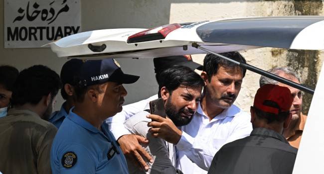 Grieving father consoles another parent as a child's coffin is carried outside PIMS Hospital following a fire that killed 14 infants in Islamabad.