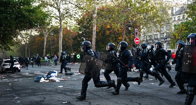 French police officers run through a street during violent clashes at Place de la République in Paris following nationwide protests over the cost of living on 18 October 2026.
