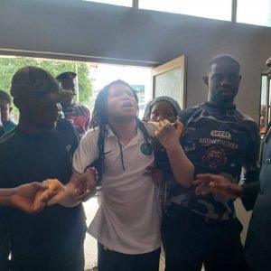 Ikechukwu Ezenagu, popularly known as Muomiri Afuluanya, being assisted by security operatives as he appears before an Anambra State High Court in Awka.
