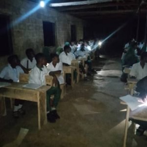 WAEC candidates writing examination papers at night using torchlights and phone flashlights after delays in the arrival of exam materials.