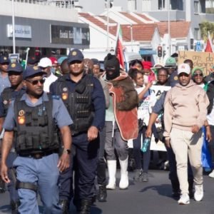 South African police officers escort anti-illegal immigration protesters carrying national flags during a march in Cape Town ahead of a June 30 migrant deadline.