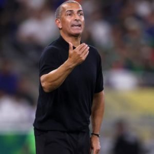 Tunisia head coach Sabri Lamouchi on the touchline during World Cup match action against Sweden, with players reacting after defeat.